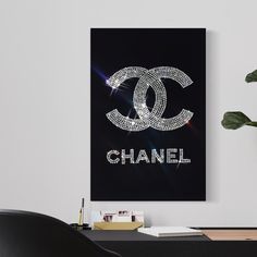 the chanel logo is displayed on a black wall above a desk with a potted plant