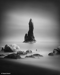 black and white photo of an ocean with rocks in the foreground, one rock sticking out of the water