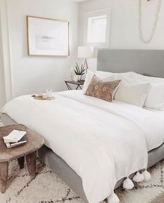 a bed with white linens and pillows in a bedroom next to a small table