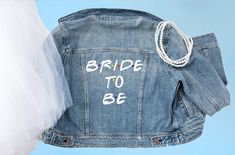 a bride to be jean jacket hanging from a line on a blue background with the words bride to be written on it