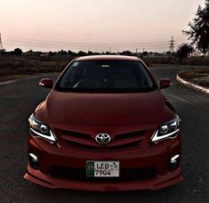 the front end of a red car parked in a parking lot next to some trees