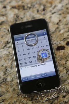 a cell phone sitting on top of a counter next to a calendar and two wedding rings