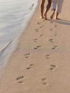 two people walking on the beach with their footprints in the sand and water behind them