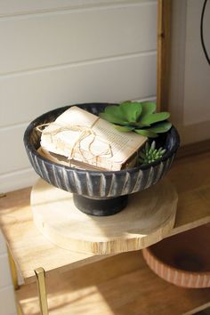 a wooden table topped with a black bowl filled with plants and an open book on top of it