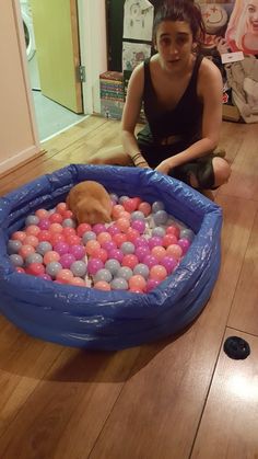 a woman sitting on the floor next to a dog in an inflatable pool