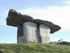 two large rocks sitting on top of a grass covered hill next to a tall rock