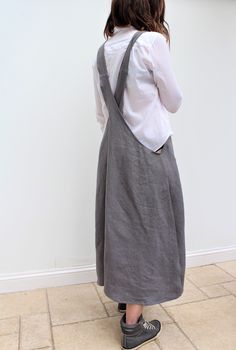 a woman standing in front of a white wall wearing a gray dress and black shoes