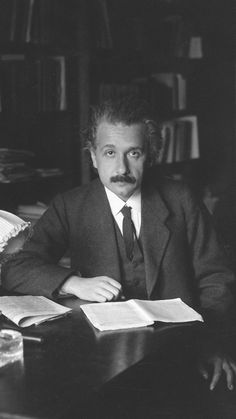 a man sitting at a desk with an open book in front of him and looking into the camera