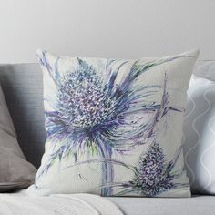 a blue and purple flower on a white background pillow sitting on top of a couch