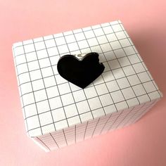 a black heart shaped object sitting on top of a white box with a pink background