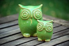 two green owl figurines sitting on top of a wooden table next to each other