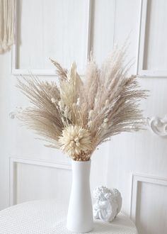 a white vase filled with dried flowers on top of a table