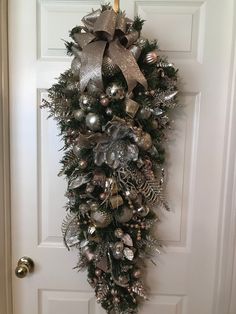 a wreath hanging on the front door decorated with silver and silver christmas balls, pineconis, bells and ornaments