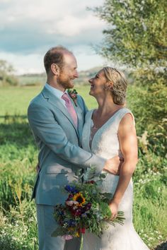 a bride and groom are standing in the grass looking into each other's eyes