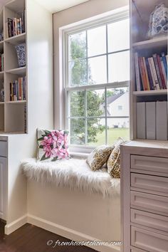 a window seat with bookshelves in the background and a pink flower pillow on it