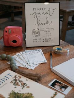 a wooden table topped with books and a pink camera next to a sign that says photo guest book