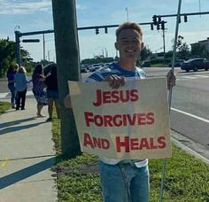 a man holding a sign that says jesus forgings and heals