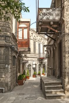 an alley way with stone buildings and steps leading up to the second floor, surrounded by potted plants