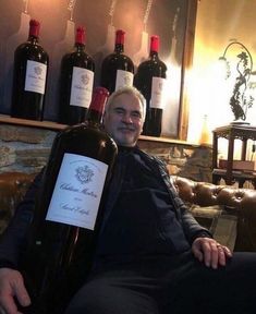 a man sitting on a couch holding a bottle of wine in front of several bottles