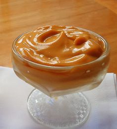 a glass bowl filled with caramel sauce on top of a white napkin next to a wooden table