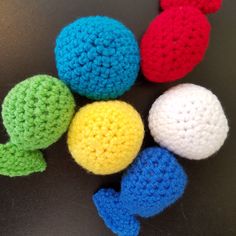 four crocheted toys are arranged in a circle on a black surface, one is red, one is green and the other is blue