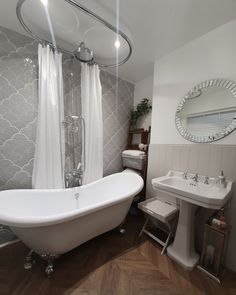 a white bath tub sitting next to a sink in a bathroom under a round mirror