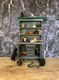 a miniature book shelf with books and other items in it on a wooden table next to a black cat