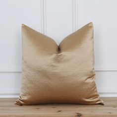 a gold pillow sitting on top of a wooden floor next to a white painted wall