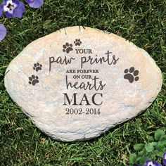 a stone with paw prints on it in the grass next to purple flowers and blue pansies