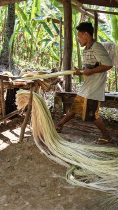 a man is weaving some kind of grass on the ground in front of his hut