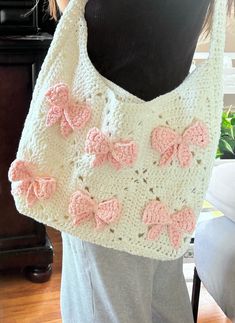 a crocheted bag with pink bows on the front and bottom, hanging from a mannequin's torso