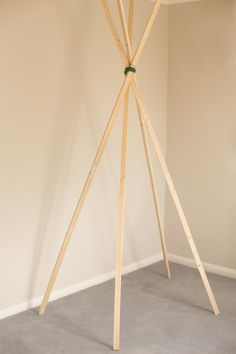 a wooden tripod stands in the corner of a room with white walls and carpet