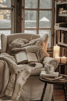 an open book is sitting on a chair in front of a window with candles and books