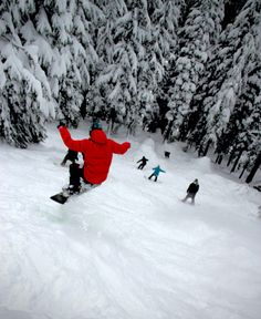 a snowboarder in red jacket doing a trick on snowy slope with trees behind him