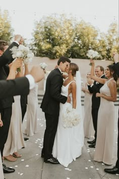 a bride and groom kissing in front of their wedding party with confetti on the ground