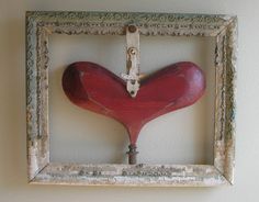 a red heart hanging on a white wall in an old wooden frame with a hook