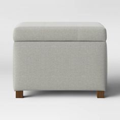 a white ottoman with wooden legs and a gray cover on it's back side