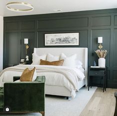 a bedroom with dark green walls and white bedding, two chairs and a couch