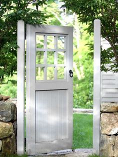 an open white door in the middle of a stone wall with trees and grass behind it