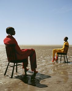 two people sitting on chairs in the water looking at each other and one person standing