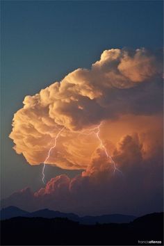 a large cloud that has lightning coming out of it and some clouds in the background