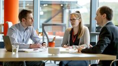 three people sitting at a table talking to each other