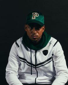 a man wearing a green and white hoodie sitting on top of a black chair