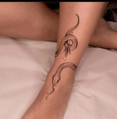 a woman's leg with a snake tattoo on it sitting on top of a bed