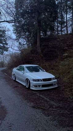 a white car parked on the side of a dirt road next to trees and bushes