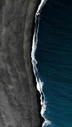 an aerial view of the ocean with black sand