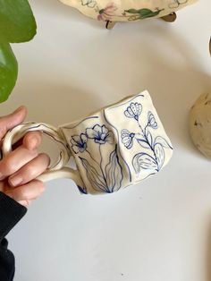 a person holding a coffee mug in front of some potted plants on a table