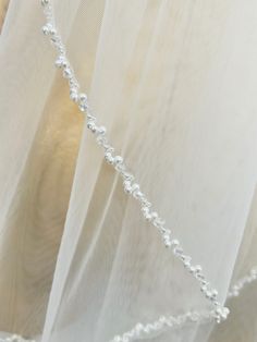 a white sheer curtain with beaded trim and pearls hanging from it's side