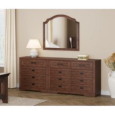 a dresser with a mirror on top of it next to a lamp and vase filled with flowers