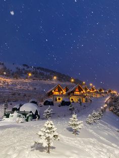 a snow covered hillside with houses and trees in the foreground, at night time